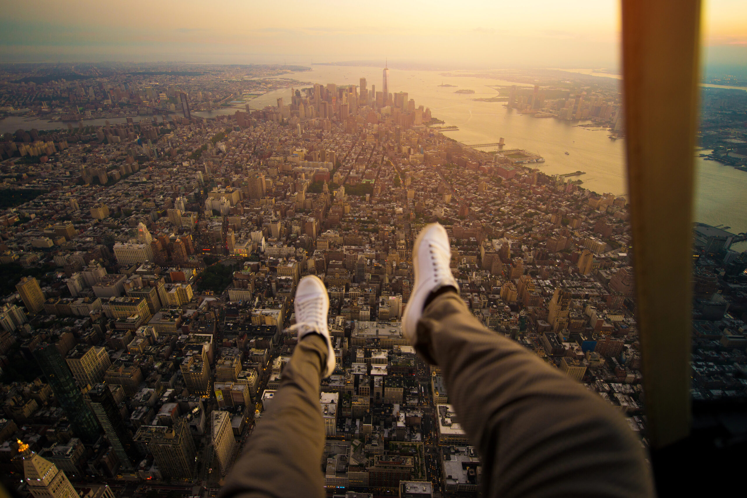 feet hanging out of helicopter over NYC skyline at sunset