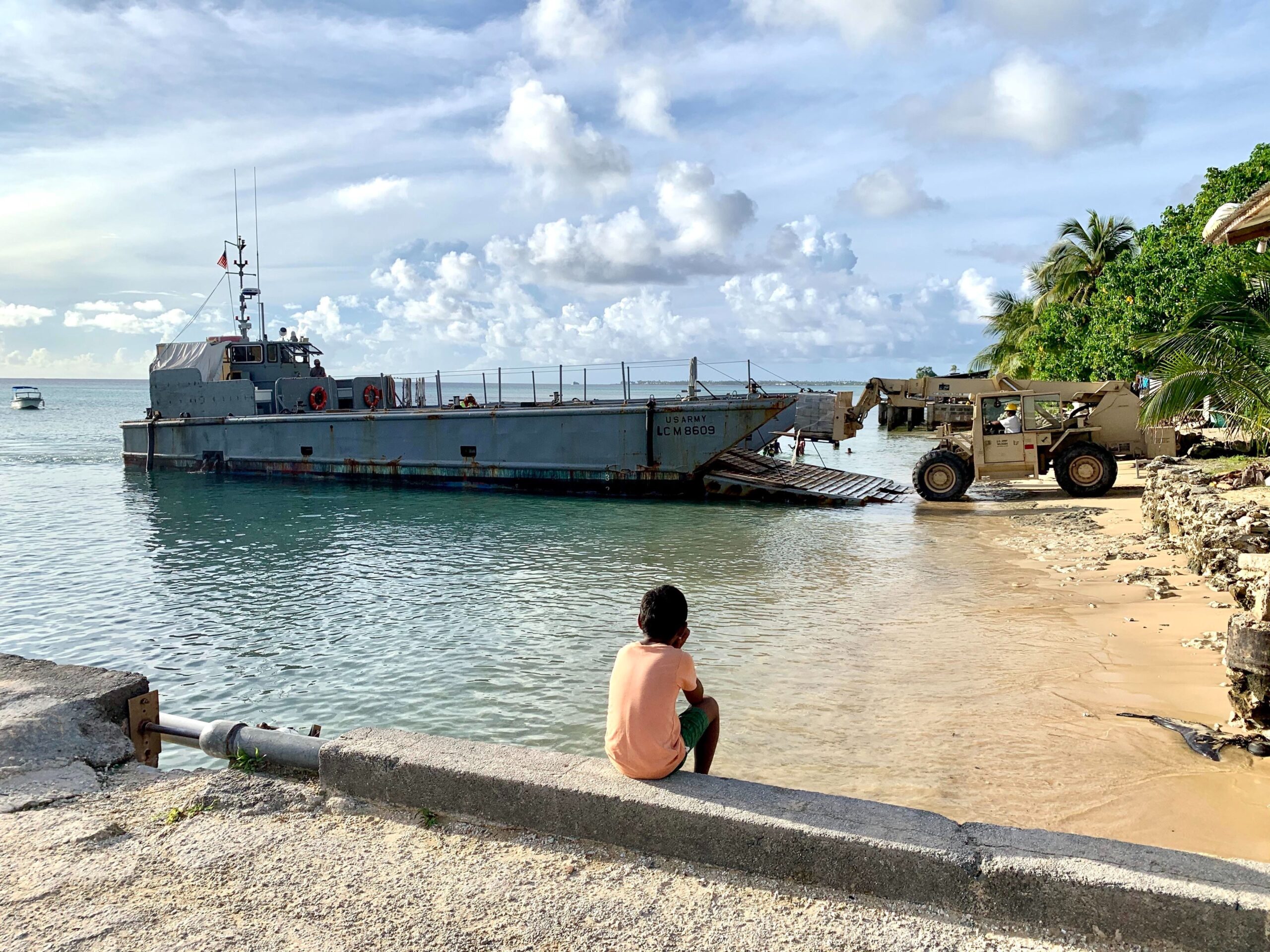 ENNIBUR, Marshall Islands (Oct. 26, 2019) A Marshall Islander watches a forklift offload materials and tools to be used by Seabees assigned to Civic Construction Action Detail Marshall Islands, deployed with Naval Mobile Construction Battalion (NMCB) 5 on Enniburr Islet on Kwajalein Atoll in the Republic of Marshall Islands. U.S. Navy Seabees deployed with NMCB-5’s Detail Marshall Islands are constructing a concrete evacuation center that will serve as the Enniburr local community’s disaster preparedness building. NMCB-5 is deployed across the Indo-Pacific region conducting high-quality construction to support U.S. and partner nations to strengthen partnerships, deter aggression, and enable expeditionary logistics and naval power projection. (U.S. Navy photo by Construction Electrician 3rd Class Christian Carnate/Released) 191026-N-PG340-1003