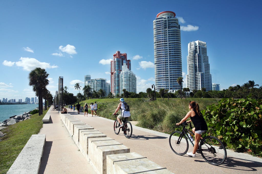 Cyclists ride along a scenic path in Miami Beach, with skyscrapers in the background.